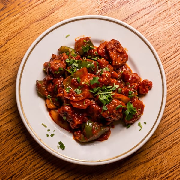 Red saucy stir-fry with bell peppers and fresh cilantro on a white plate.