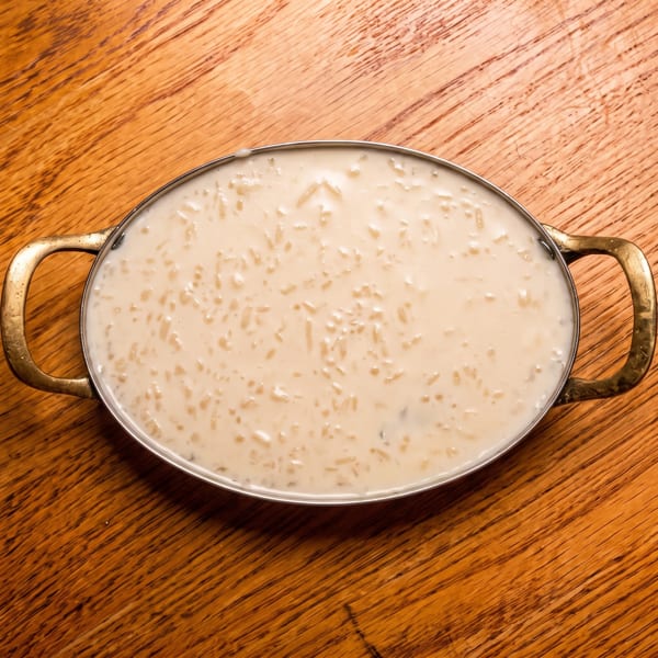 Oval metal pan filled with creamy rice pudding on a wooden table.