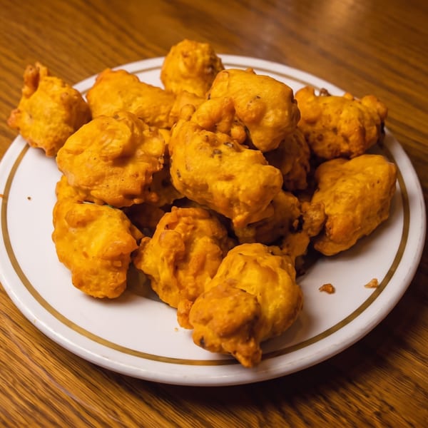 Golden-brown fried pakoras piled on a white plate with a gold rim on a wooden table.